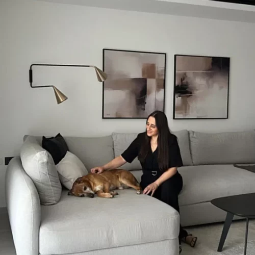 Woman relaxing with golden dog on gray sectional sofa in minimalist living room.